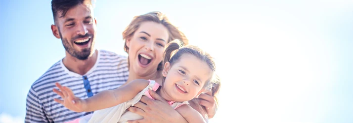 Family of three smiling against a blue sky